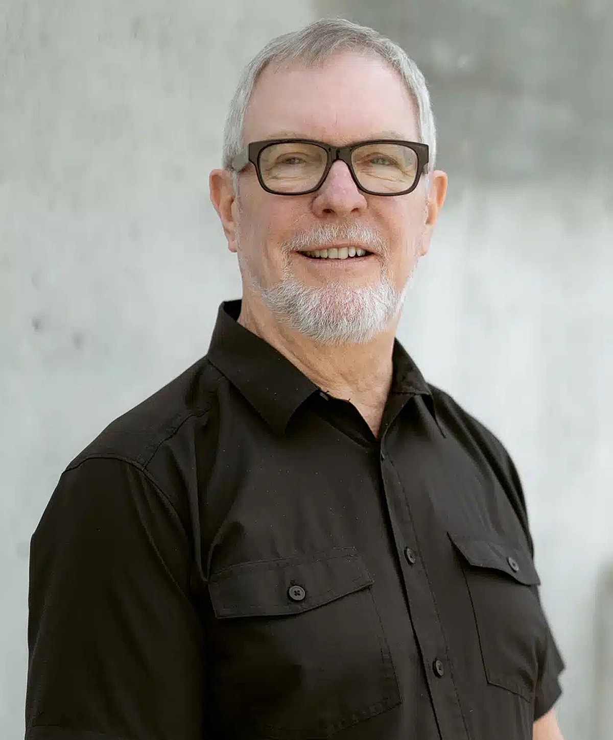 Smiling older man in a black button-up shirt.