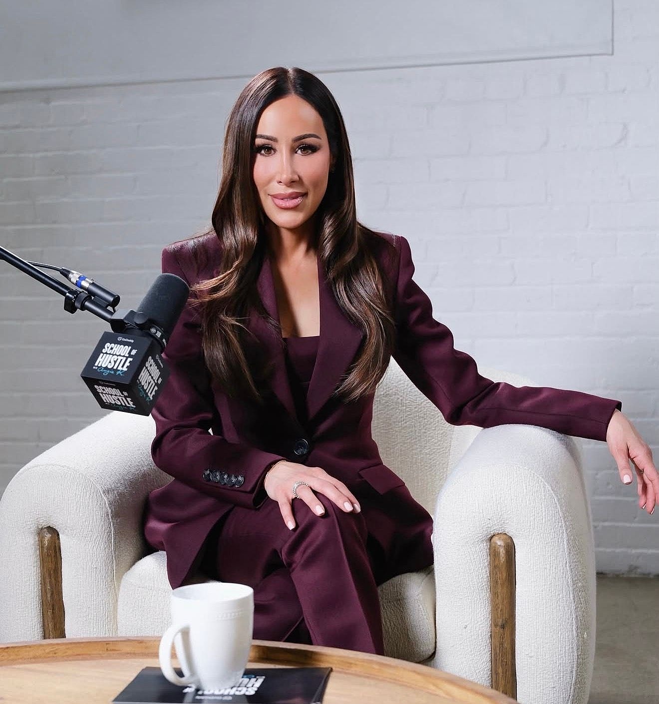 Woman in burgundy suit sitting on a chair.