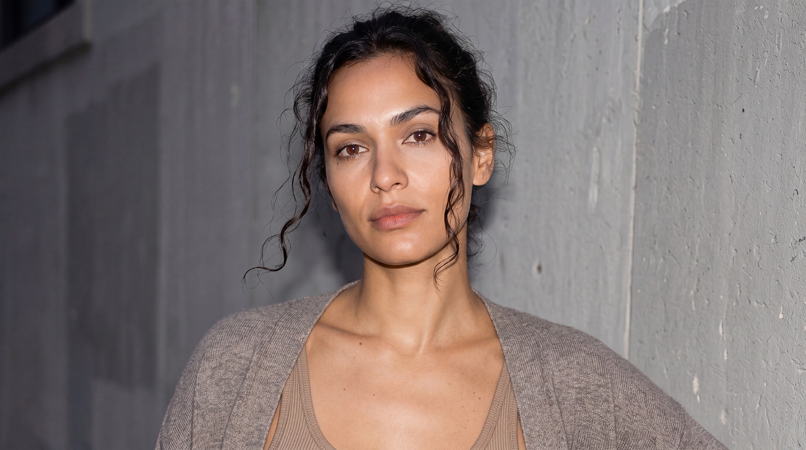 Person with wavy hair posing against a wall.