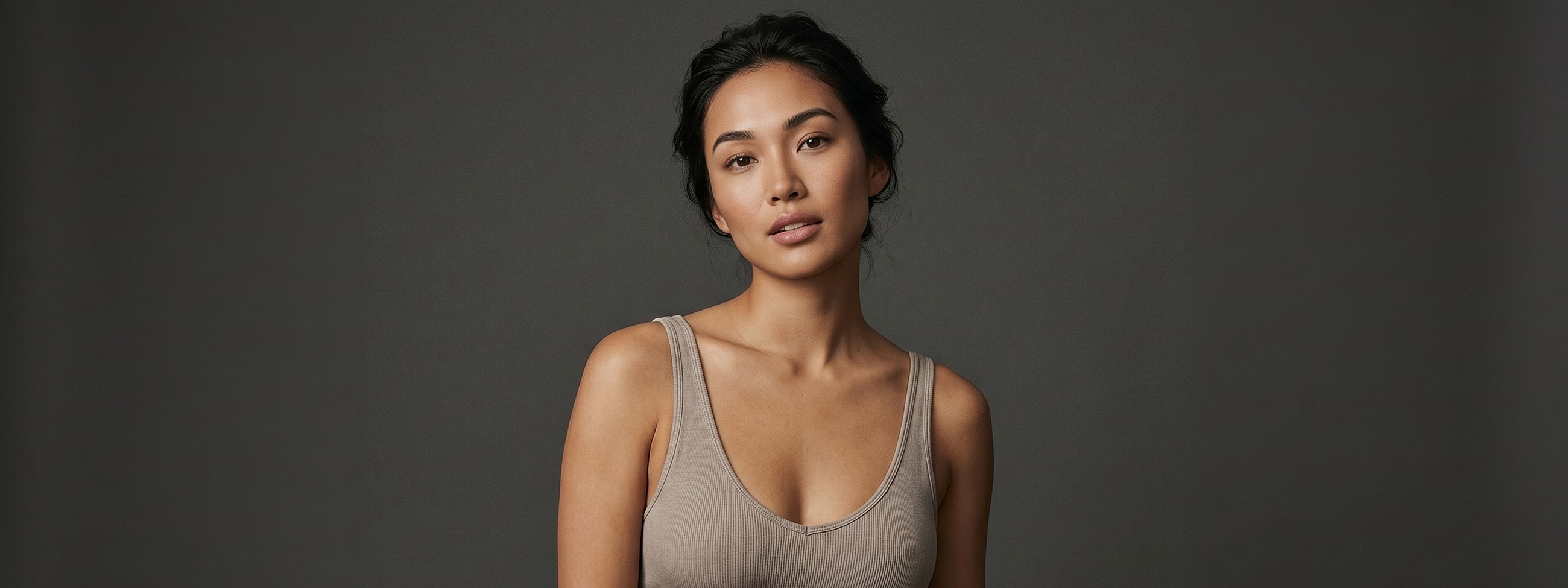Woman posing in a tank top against dark background.
